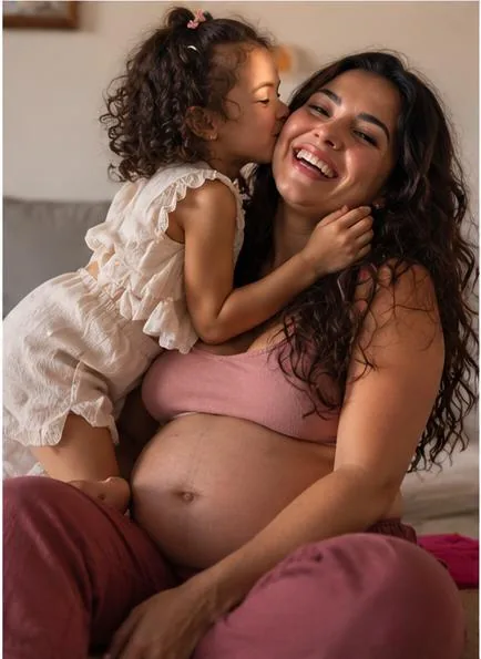 Gestante sorrindo enquanto a filha pequena beija o rosto dela